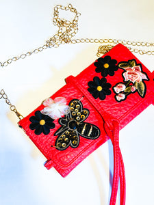Faux red leather small clutch wallet with bee and flower patches and a gold chain strap.